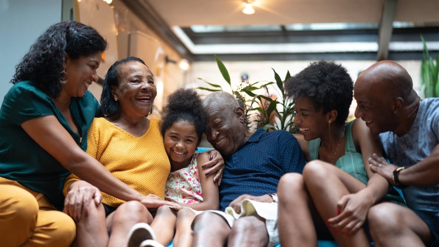 intergenerational black family laughs and hugs on a couch, pacifica senior living black history month blog header